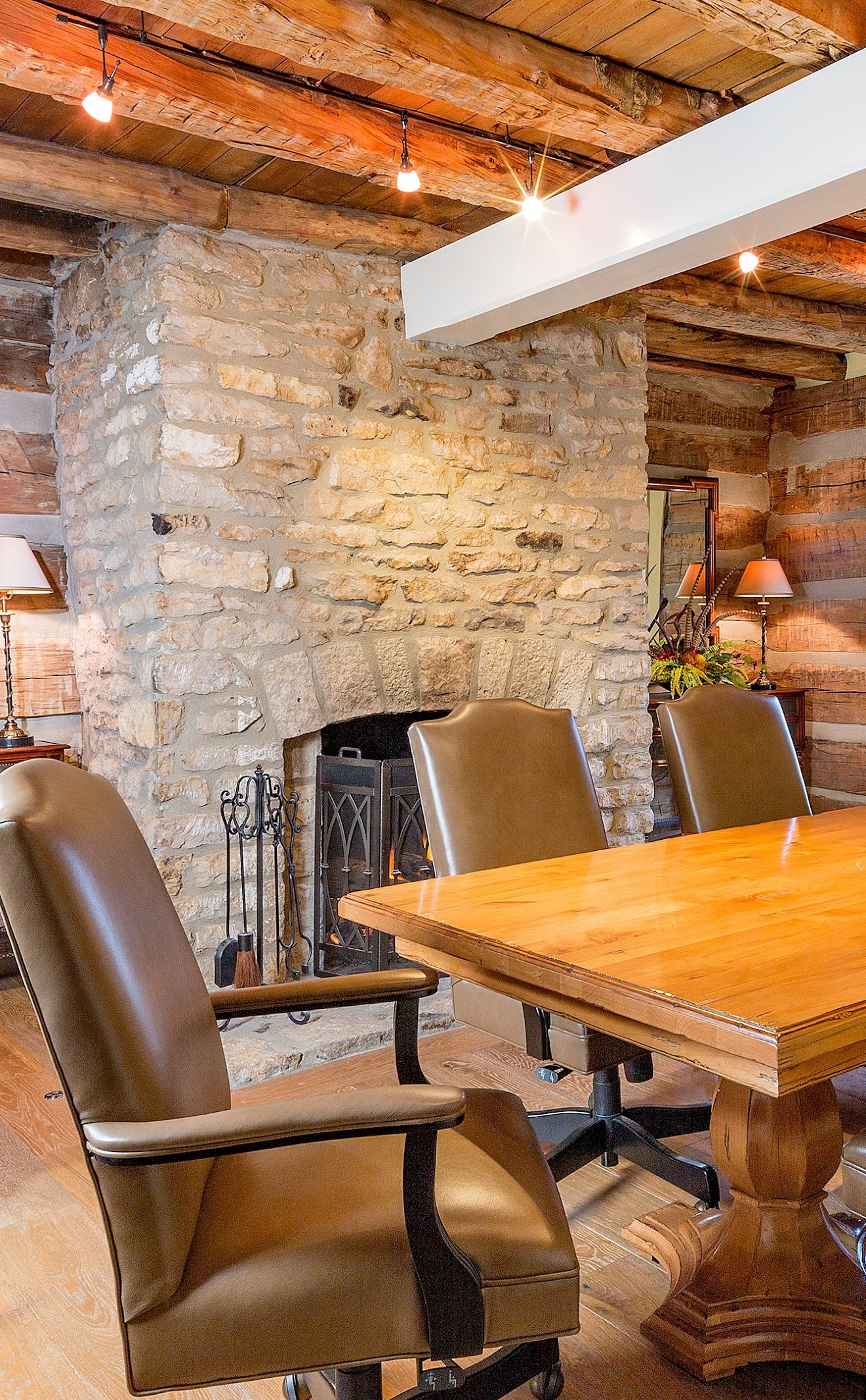 Detail of a stacked stone fireplace and leather armchairs in a warm cabin-style dining room