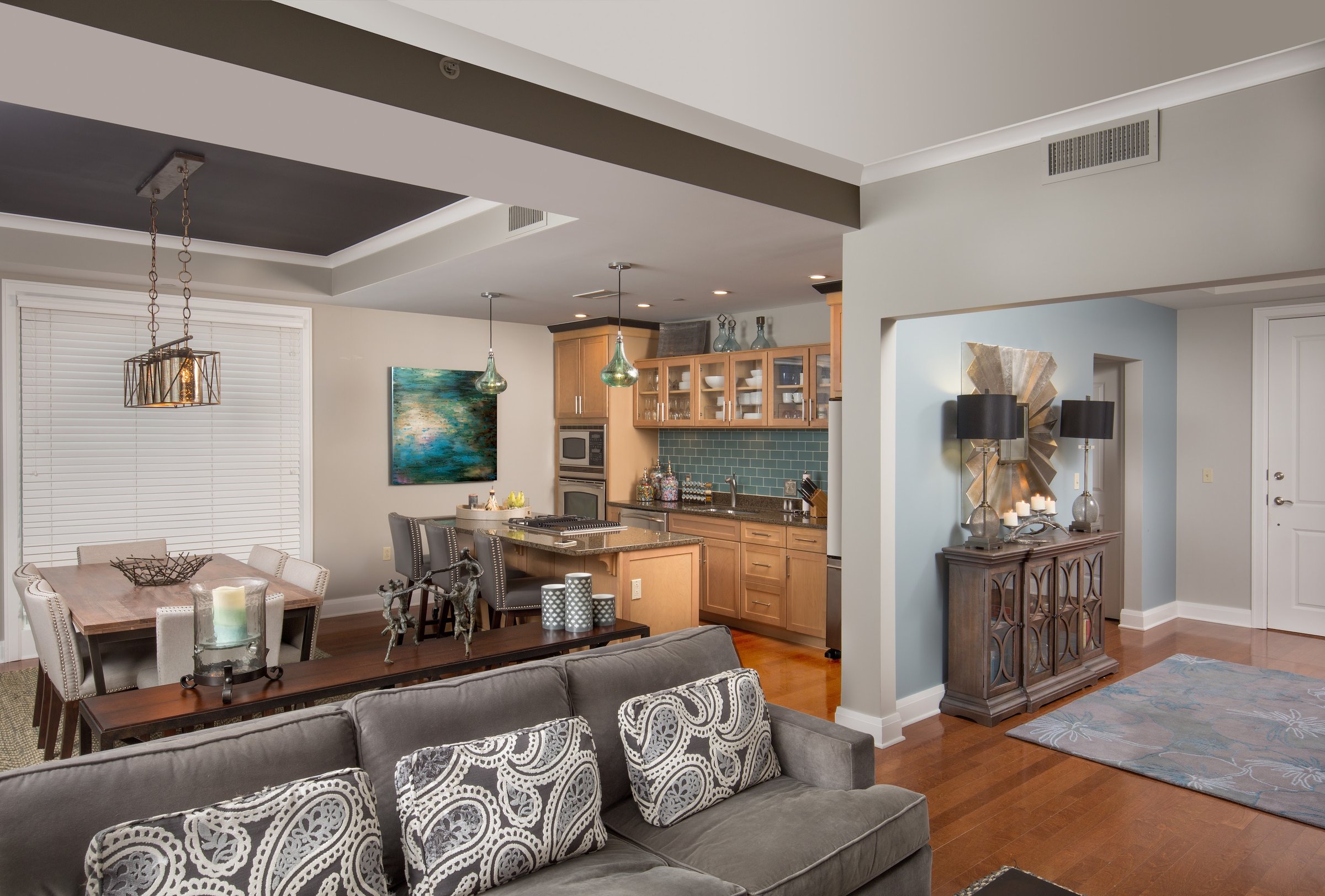 Open-concept kitchen, dining, and living space with a tiled backsplash and a sunburst mirror vignette