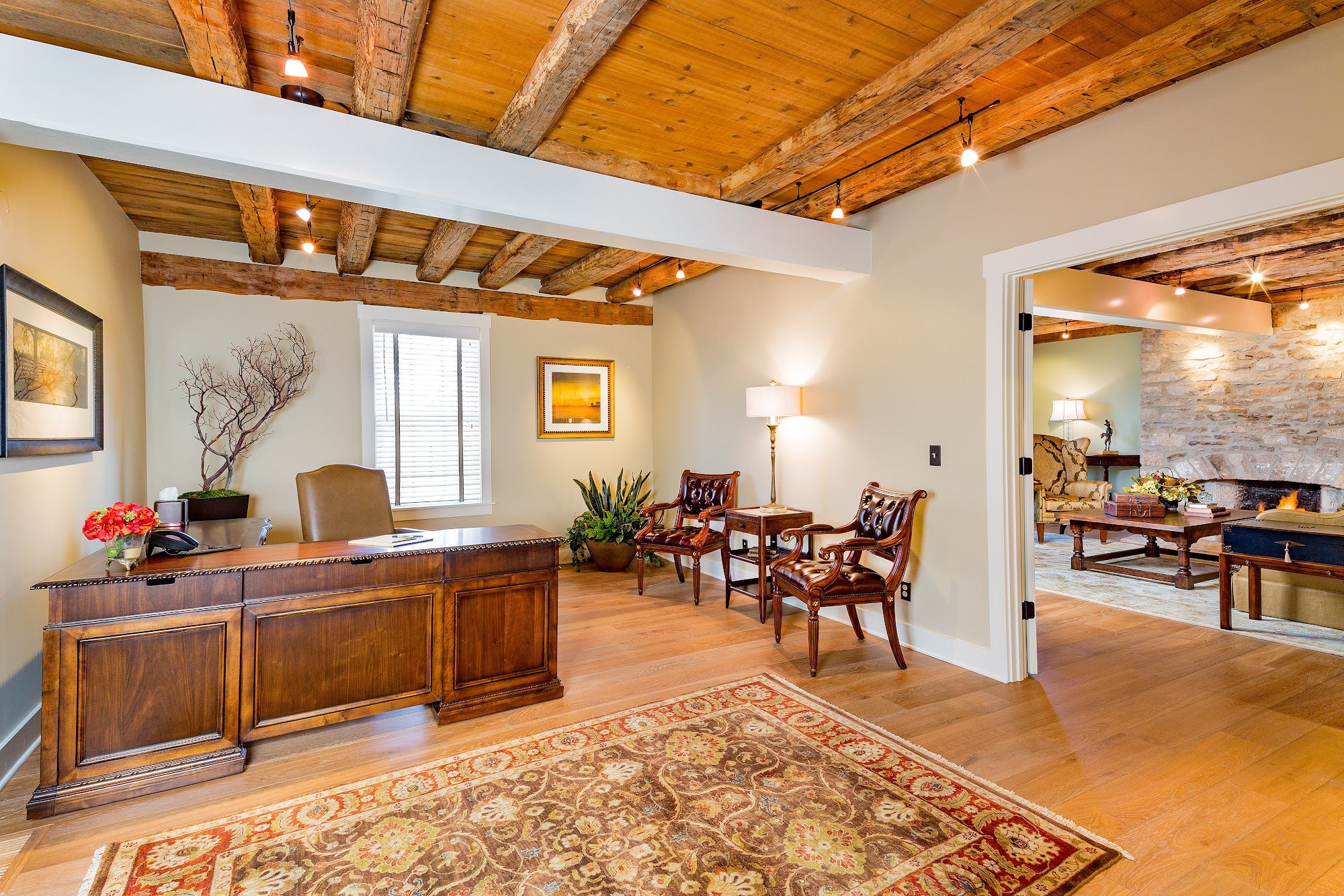 Rustic private study with a wood beam ceiling, a wooden executive desk, and leather chairs